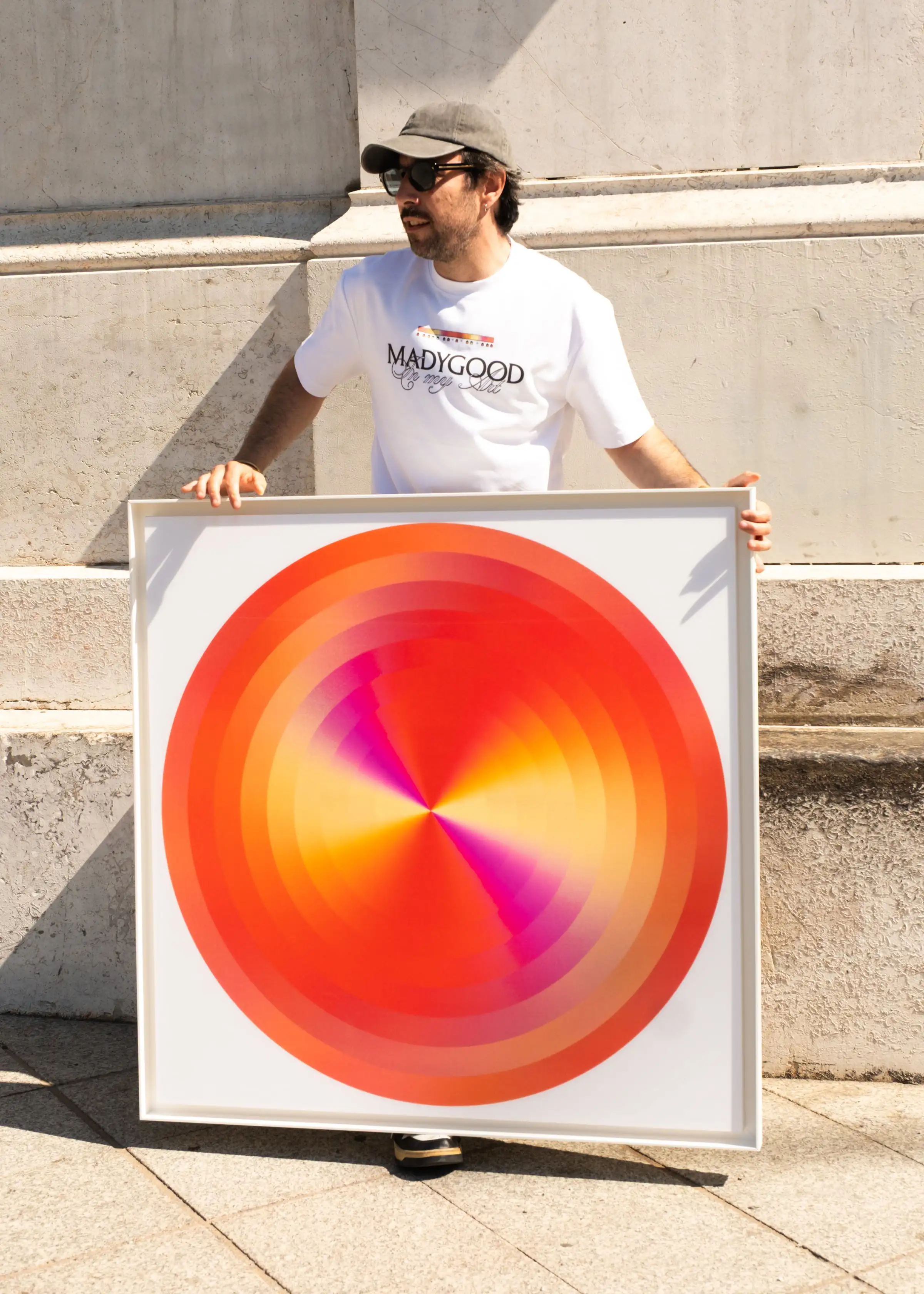 Anthony Celerier holds a circular orange artwork in a white frame, against a stone wall.